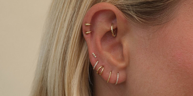 Close-up of an ear with two Patt flat backs stacked on the helix, a diamond hoop in the rook, and diamond and gold hoops through the lobe.