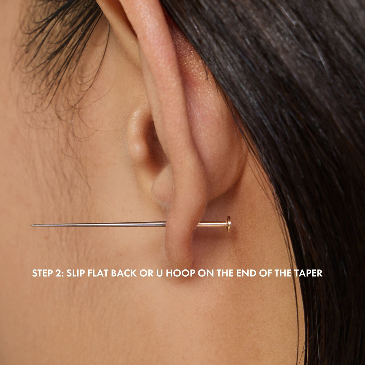 Close-up of an earlobe with a taper and printed step 2 instructions.