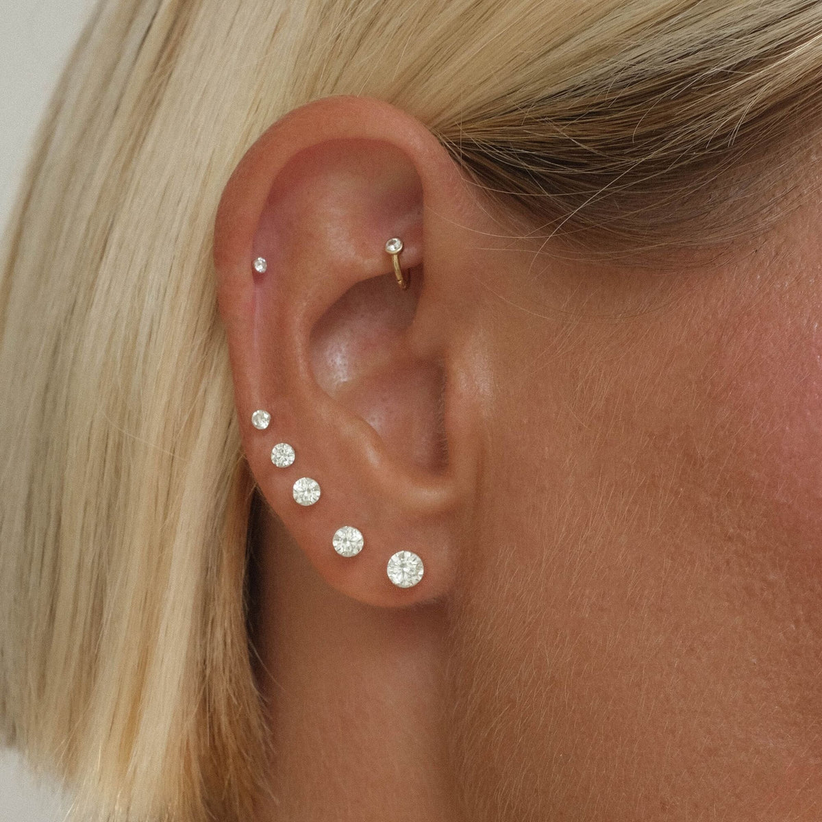 Ear styled with graduated round clear-stone studs along the lobe and small cartilage earrings.