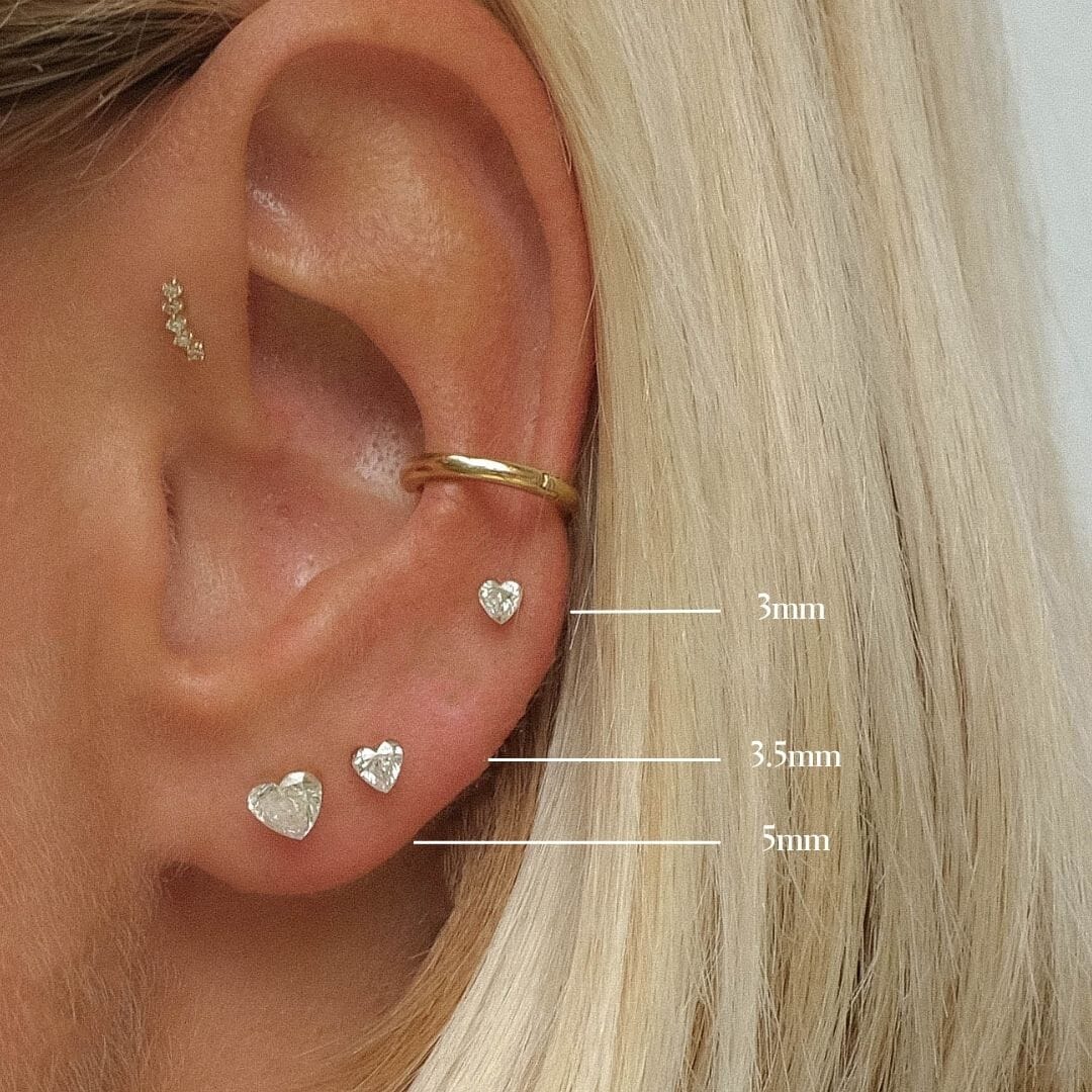 Ear wearing heart-shaped clear-stone studs in different sizes.