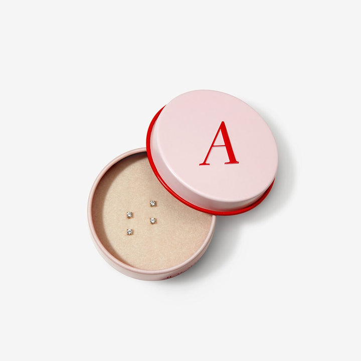Small gold diamond earrings inside an open pink round Adornmonde jewelry box.
