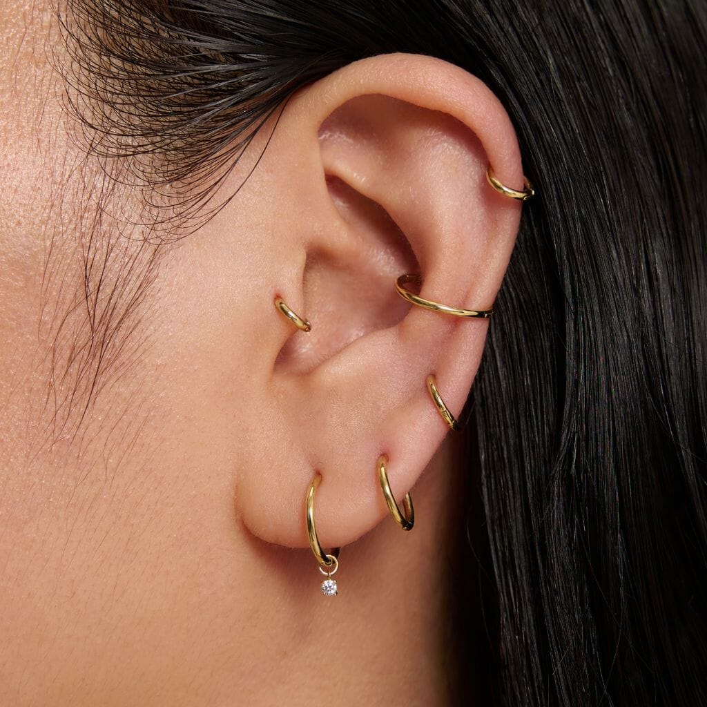 Ear stack of slim gold-tone hoops with a small clear stone charm on the lowest hoop.